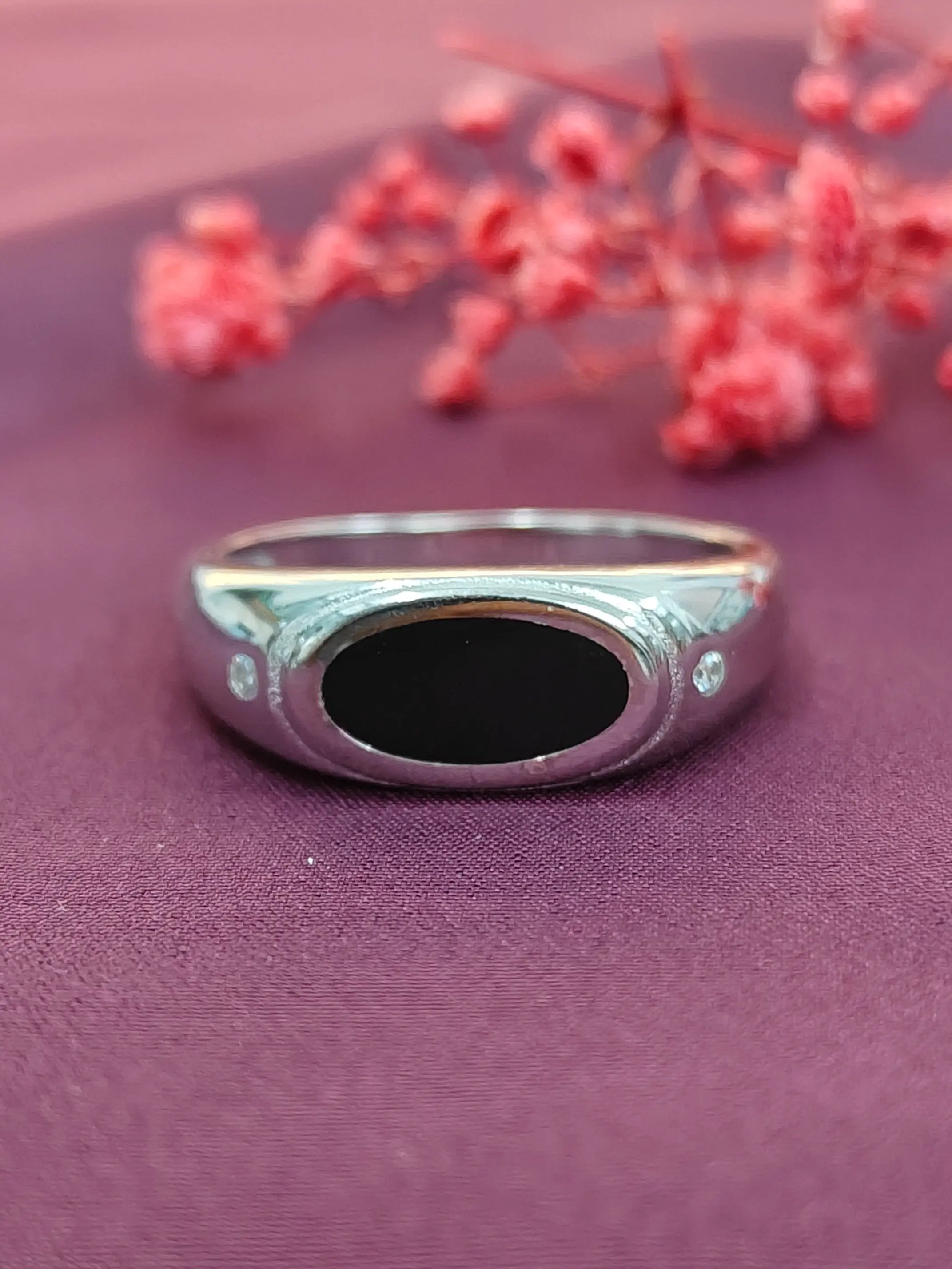 Silver ring with a black stone on a purple surface with red flowers.
